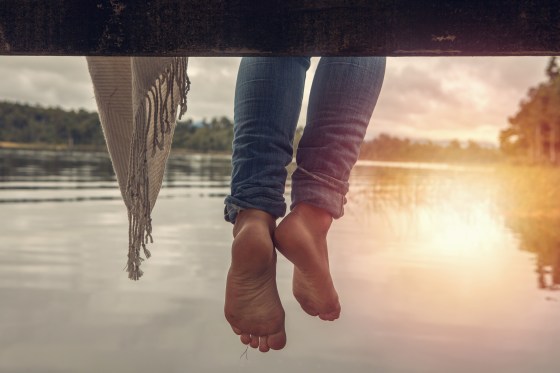 Woman's feet dangle from wooden wharf, above lake
